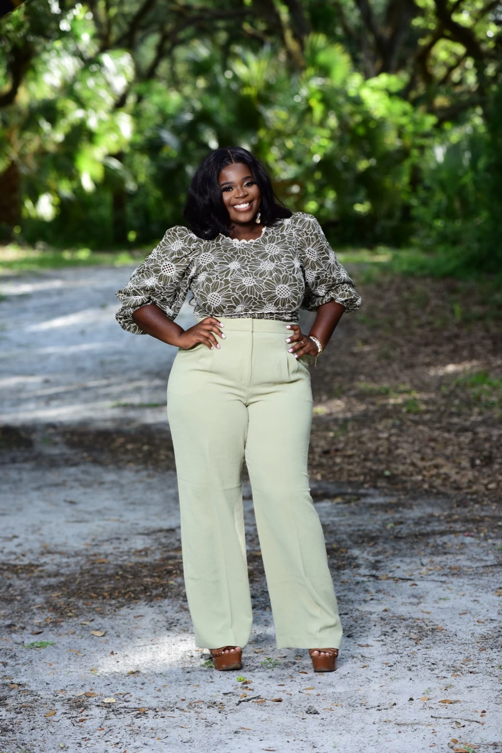 Molina Jeune-Pierre smiling on a tree-lined path in a floral blouse and light green trousers